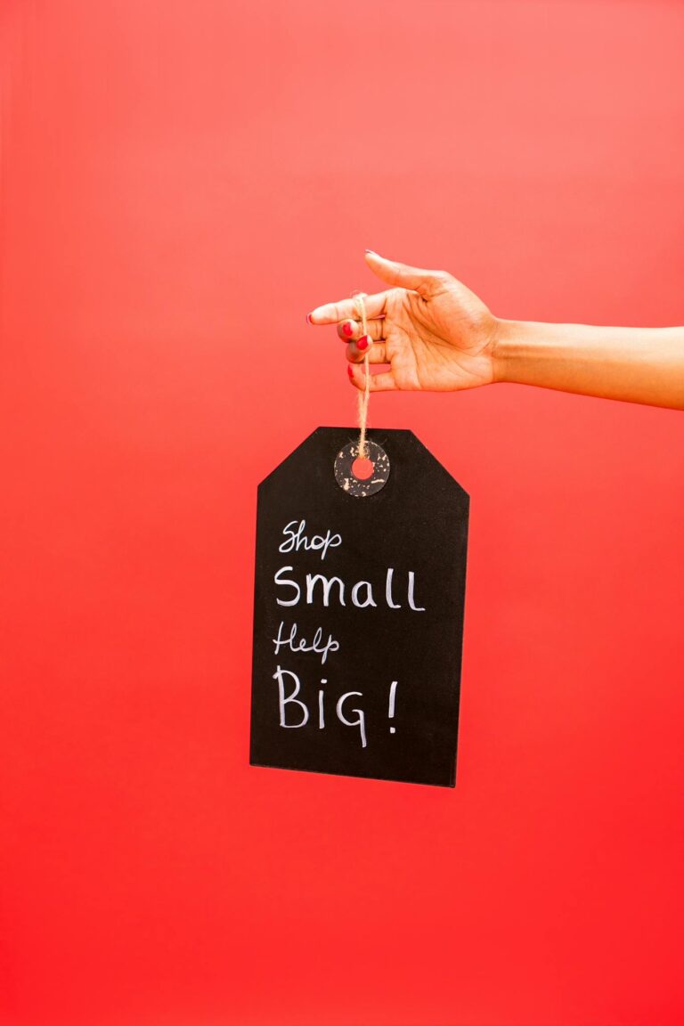 A hand holding a sign that reads 'Shop Small Help Big' against a red background.