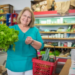 Smiling elderly woman with groceries in a store, showing fresh produce.