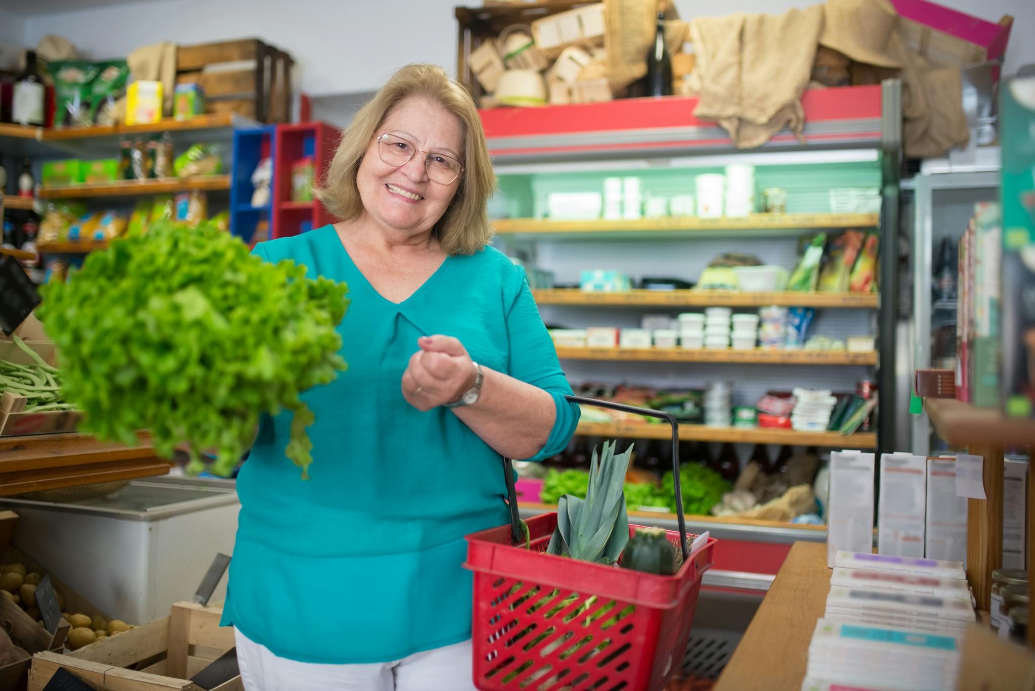 Smiling elderly woman with groceries in a store, showing fresh produce.