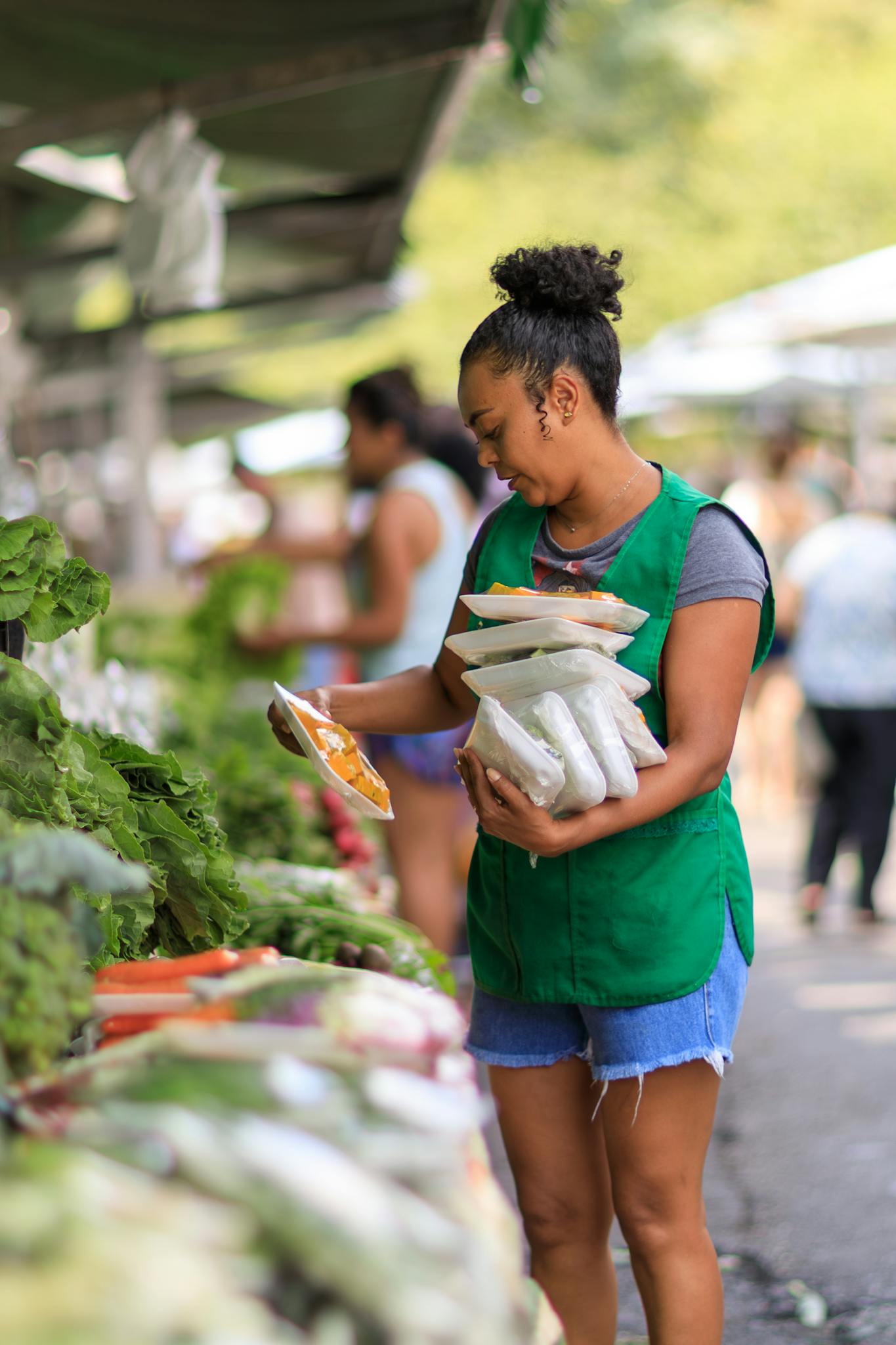 Woman arranging products at an outdoor farmer's market, showcasing fresh produce.